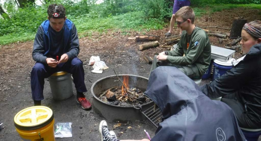 A group of students sit around a campfire. 